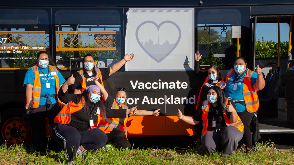Volunteers-pose-in-front-of-an-Auckland-city-vaccination-bus-at-the-Otara-Stake-Centre-drive-through-on-Super-Saturday.--New-Zealand,-2021